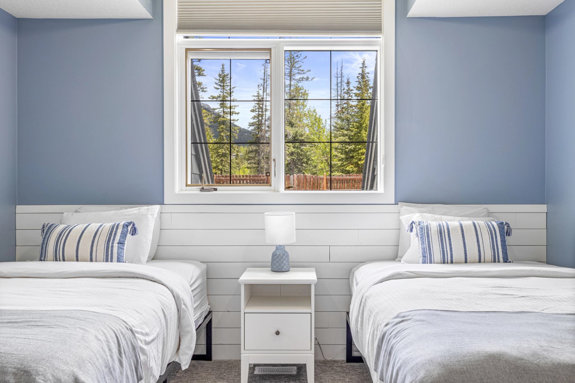 Twin beds flank a nightstand beneath a window overlooking evergreen trees.