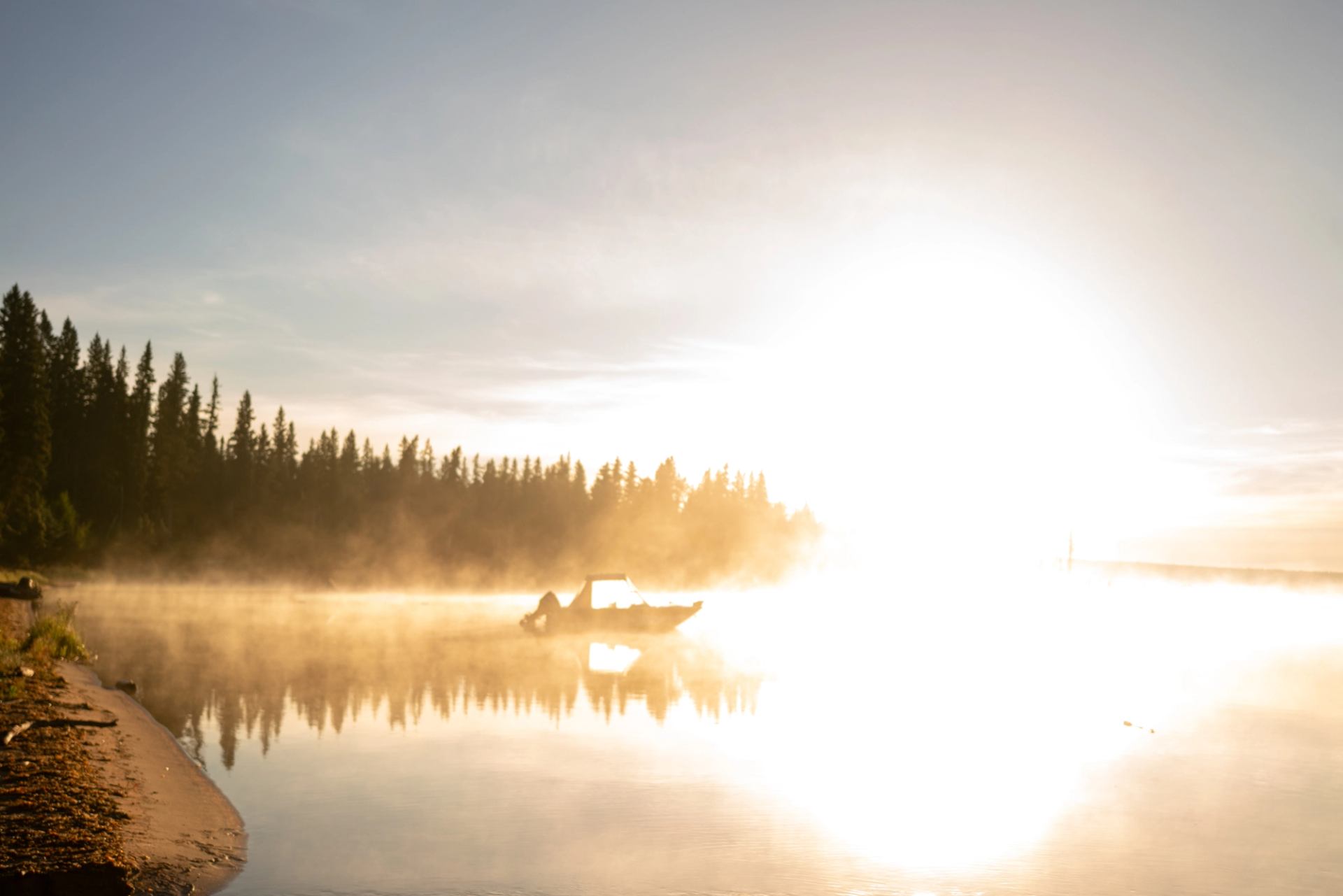 A boat on a misty lake at sunrise with a forested shoreline in the background.