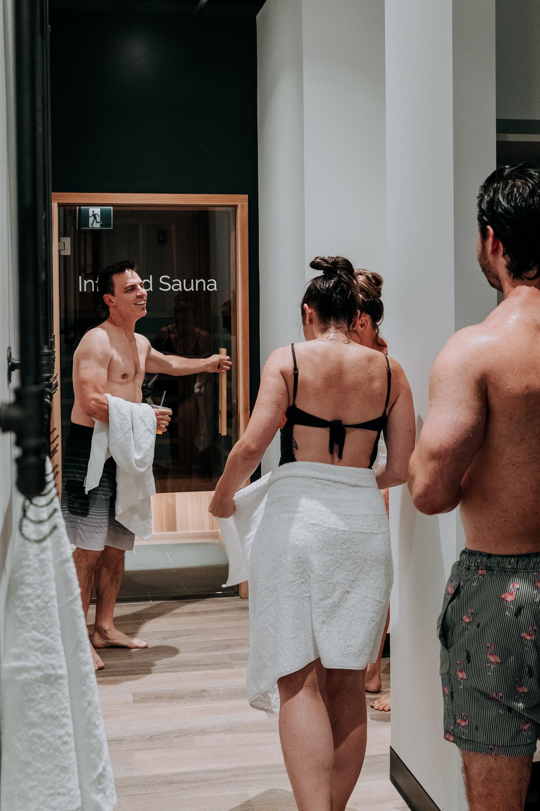 People entering a sauna in a spa setting with towels and warm lighting.