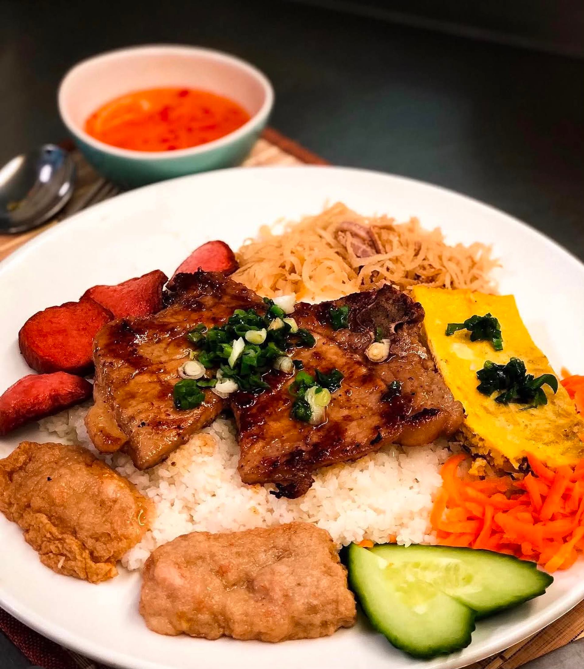 Plate of grilled pork on rice with egg, pickled vegetables and dipping sauce.
