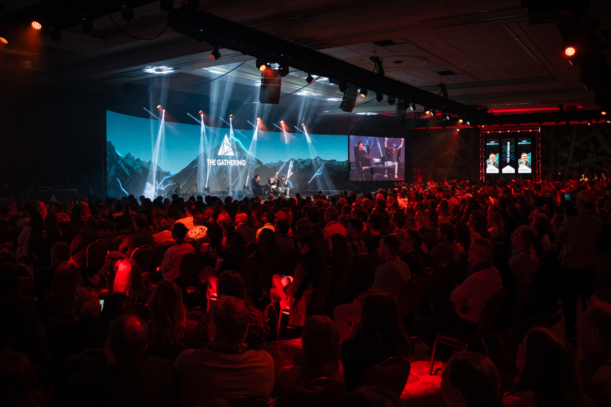 Audience in front of a stage with spotlights and screens at The Gathering Festival.