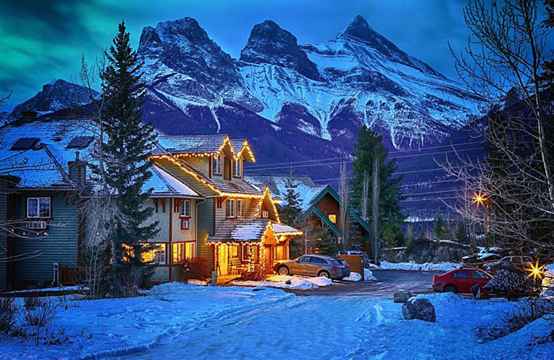 Snow‑covered lodge lit warmly with tall peaks rising in the background.