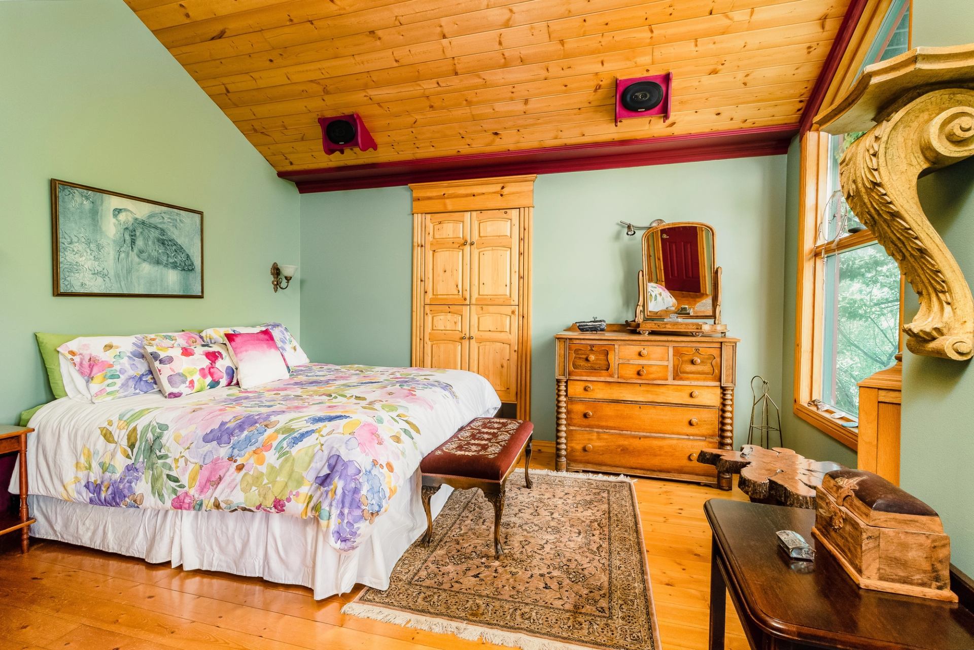 Bright bedroom with floral bedding, wood ceiling, and vintage furniture.