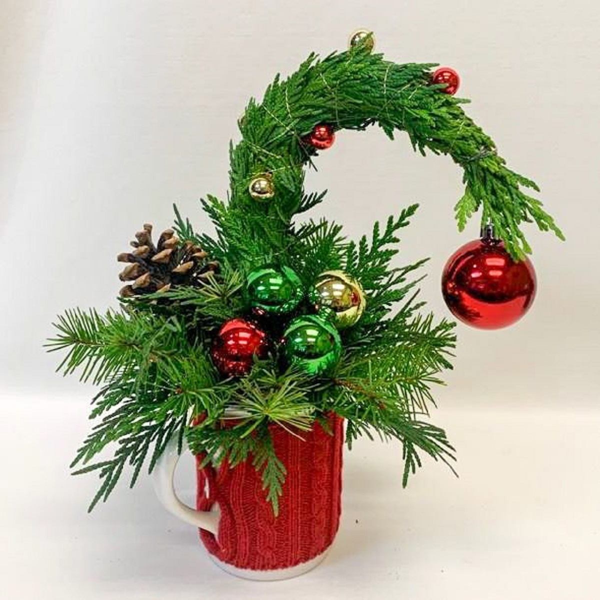 Festive pine arrangement in red mug with ornaments and curved top.