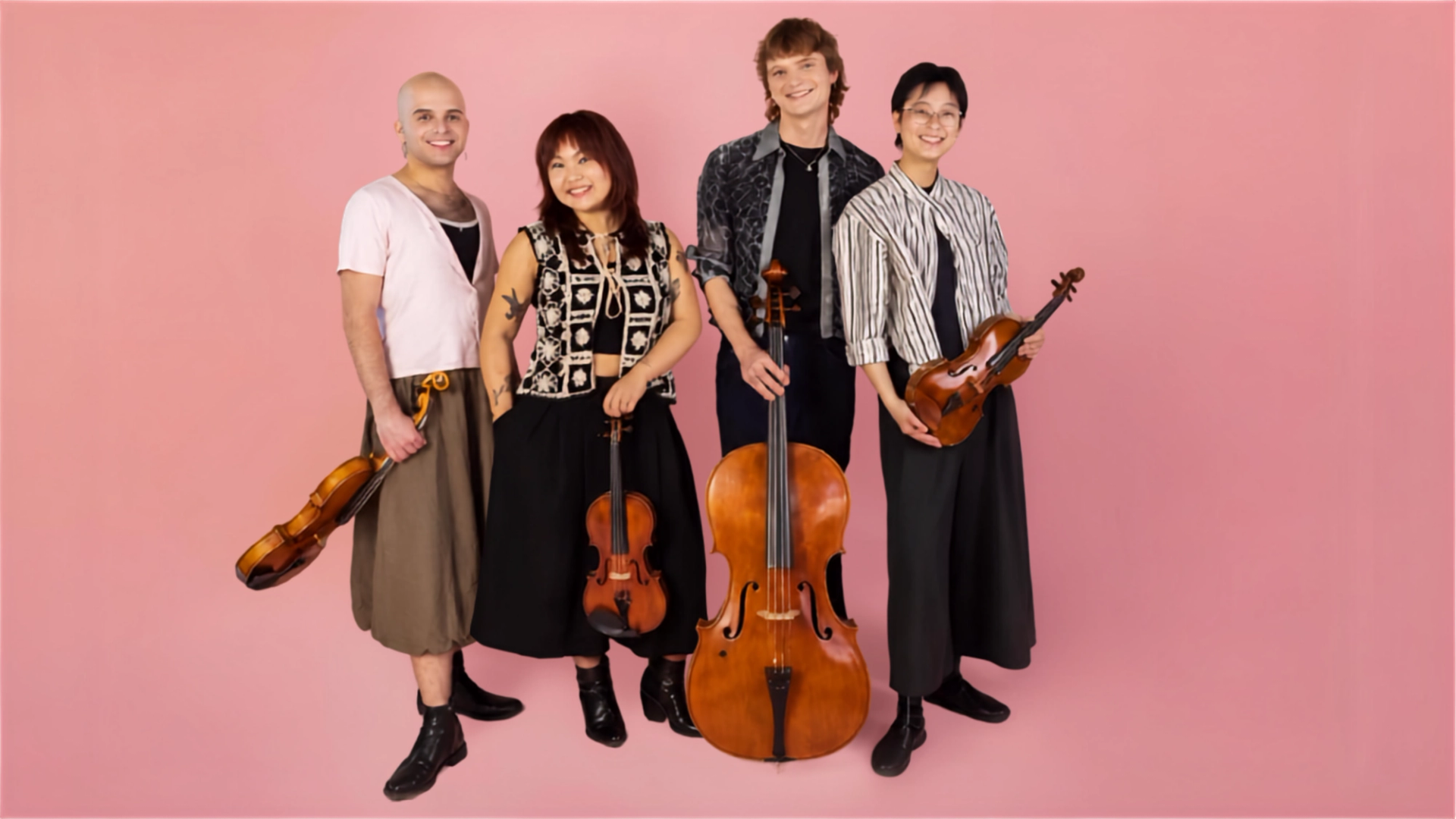 String quartet musicians stand against pink background holding violins and cello upright.