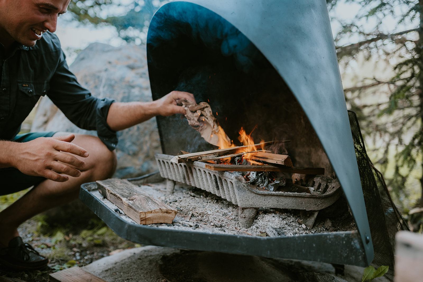 Person adds crumpled paper to a wood fire in an outdoor metal fireplace.