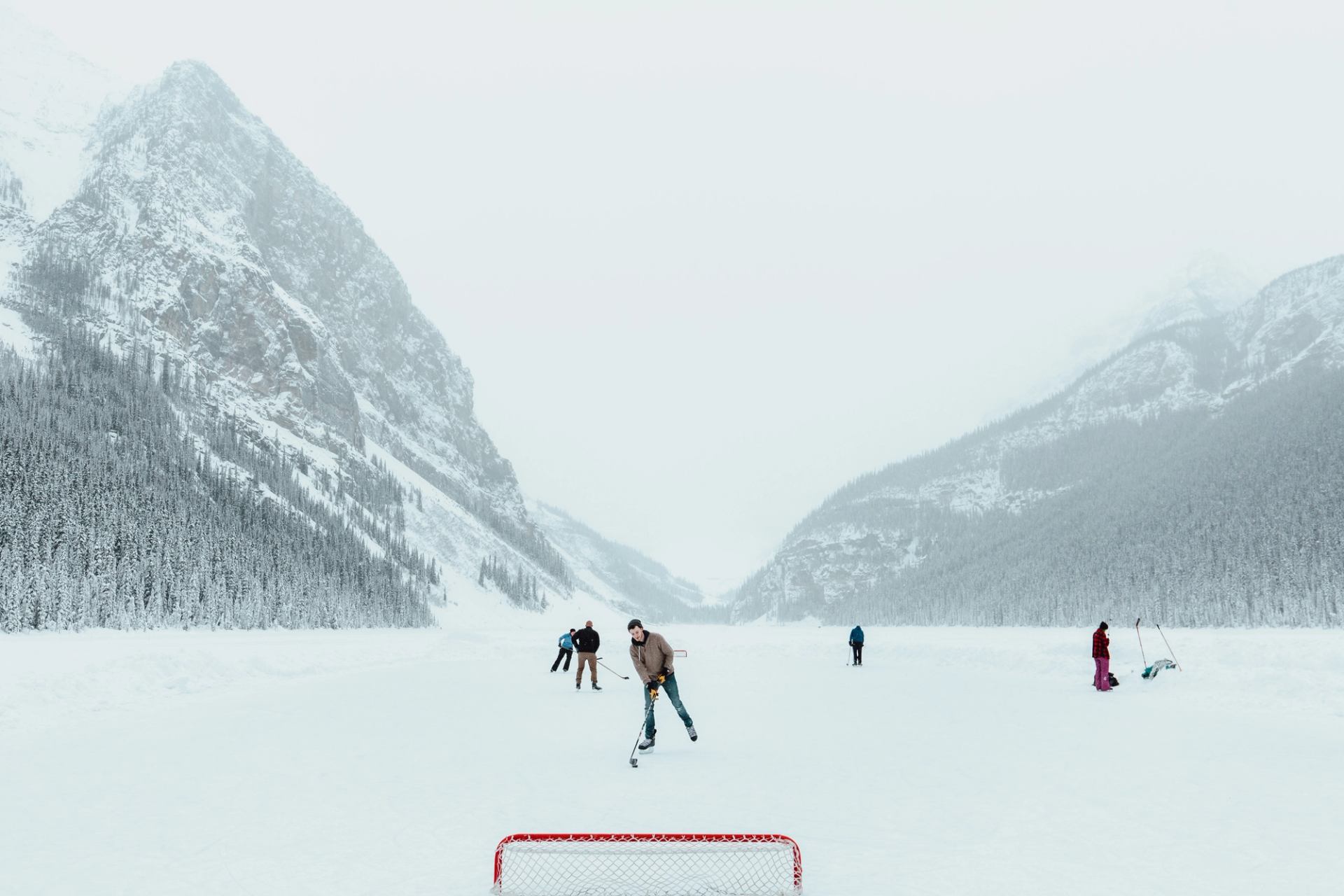 People playing hockey on a frozen lake surrounded by snowy mountains in Banff.