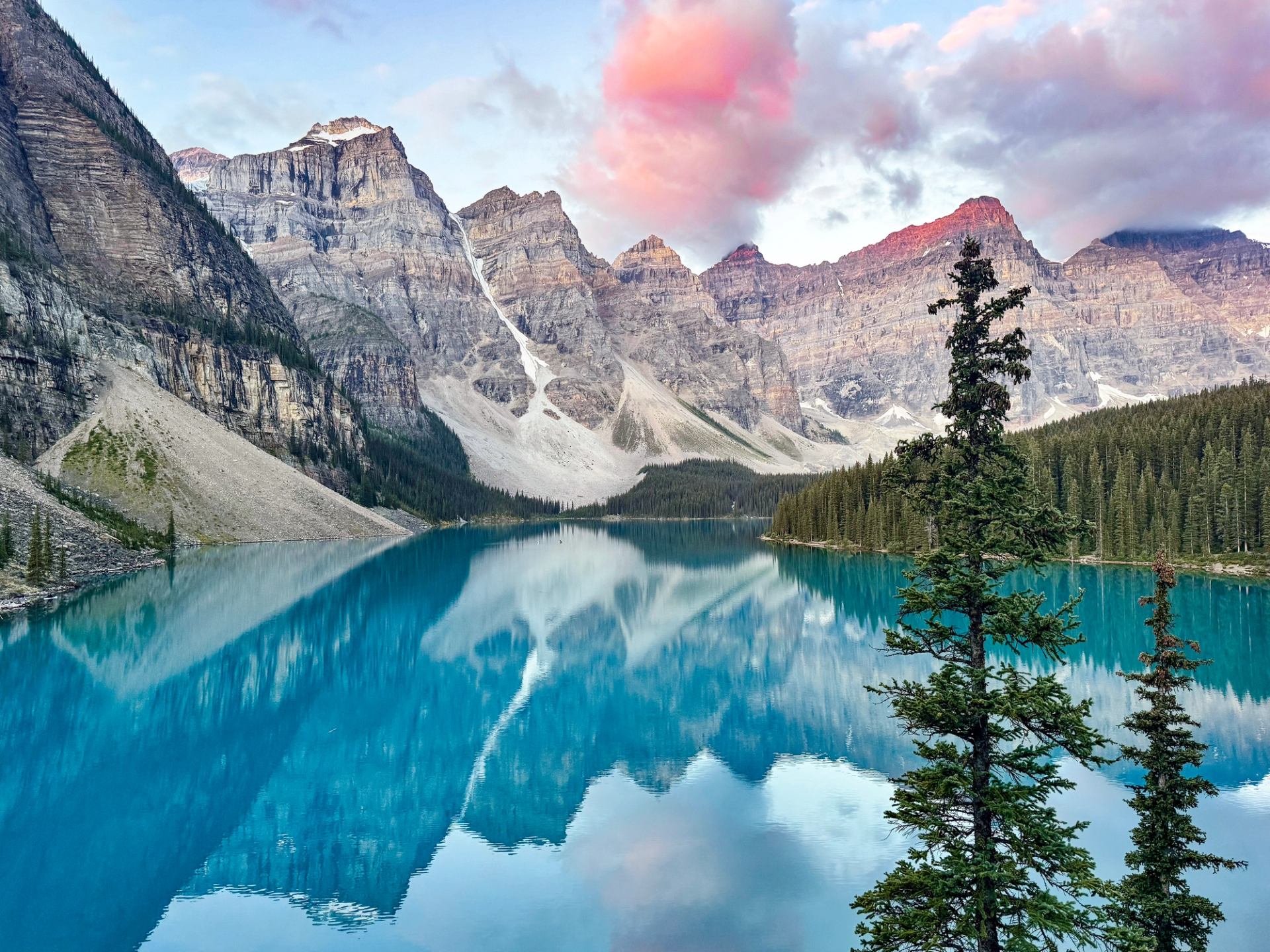 Moraine Lake with turquoise water reflecting rocky mountains under a sky with pink clouds.