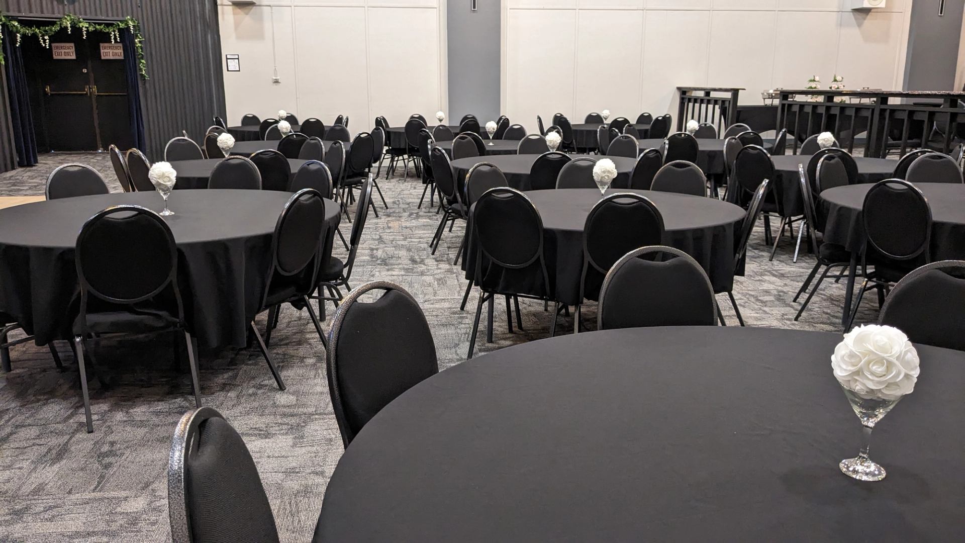 Banquet hall with round black tables and white flower centrepieces on grey carpet.