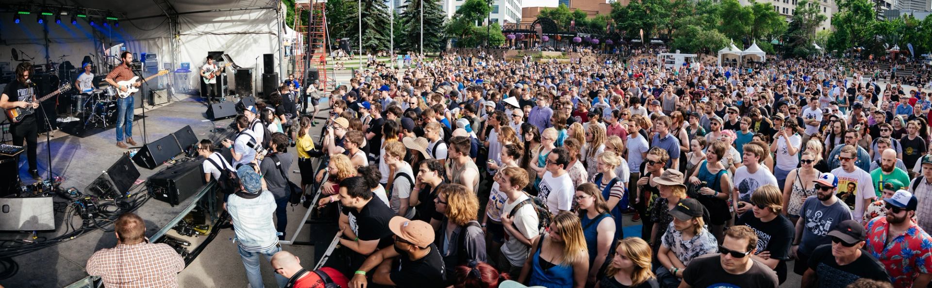 A large outdoor crowd watches bands perform on a stage during Sled Island Music & Arts Festival.