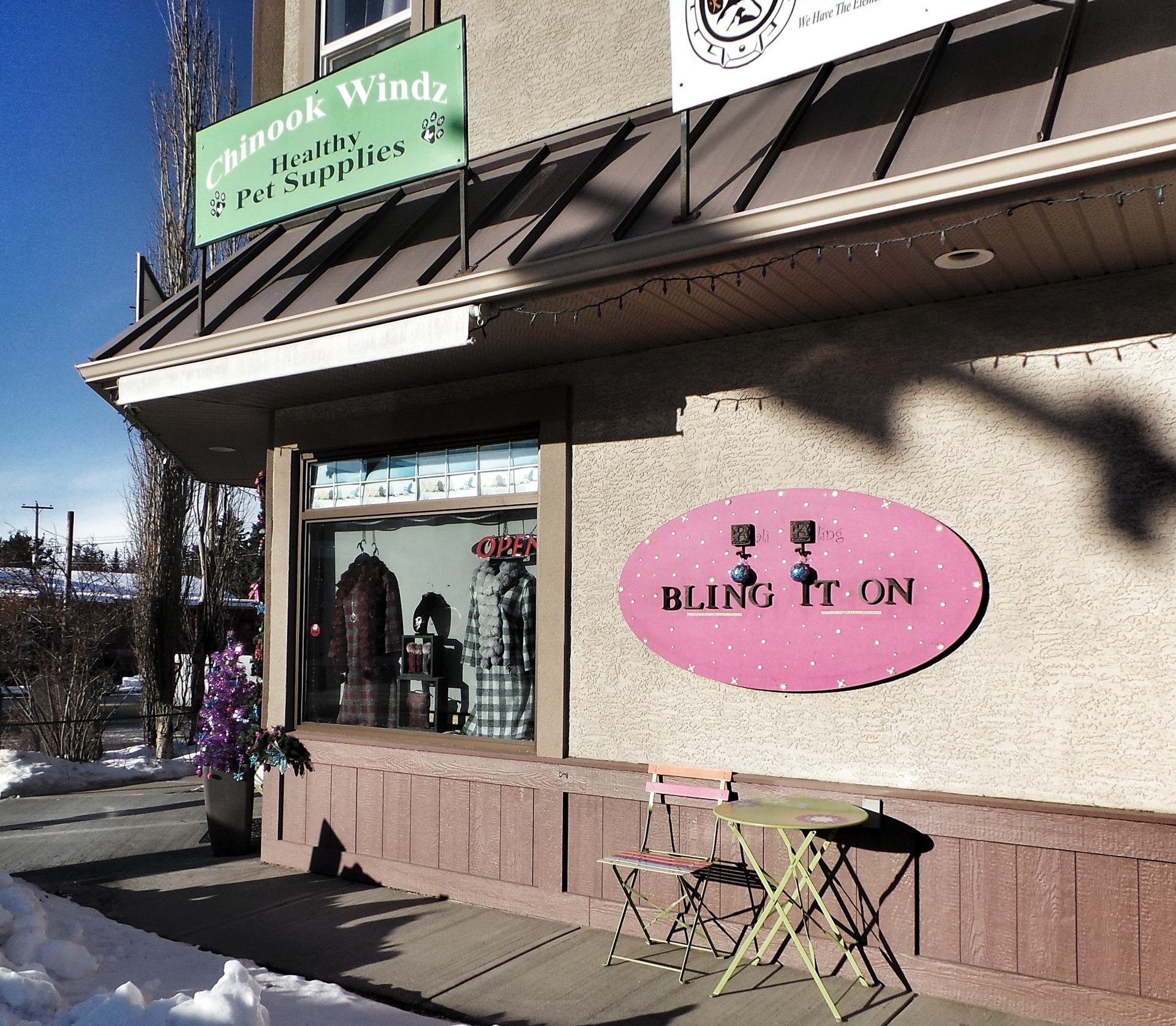 Storefront wall with "BLING IT ON" sign, window display, table and chair.