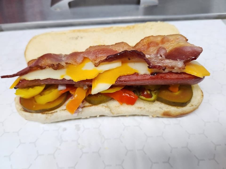 Open sandwich with bacon, sliced cheese, pickles and peppers on a bun.