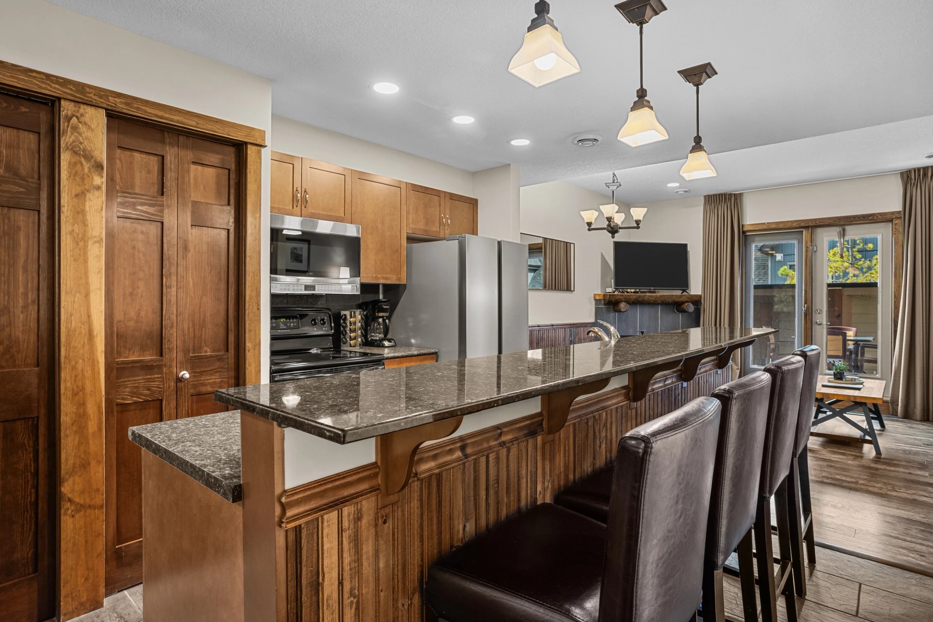 Kitchen with granite breakfast bar, leather stools, wood cabinetry and stainless steel appliances.