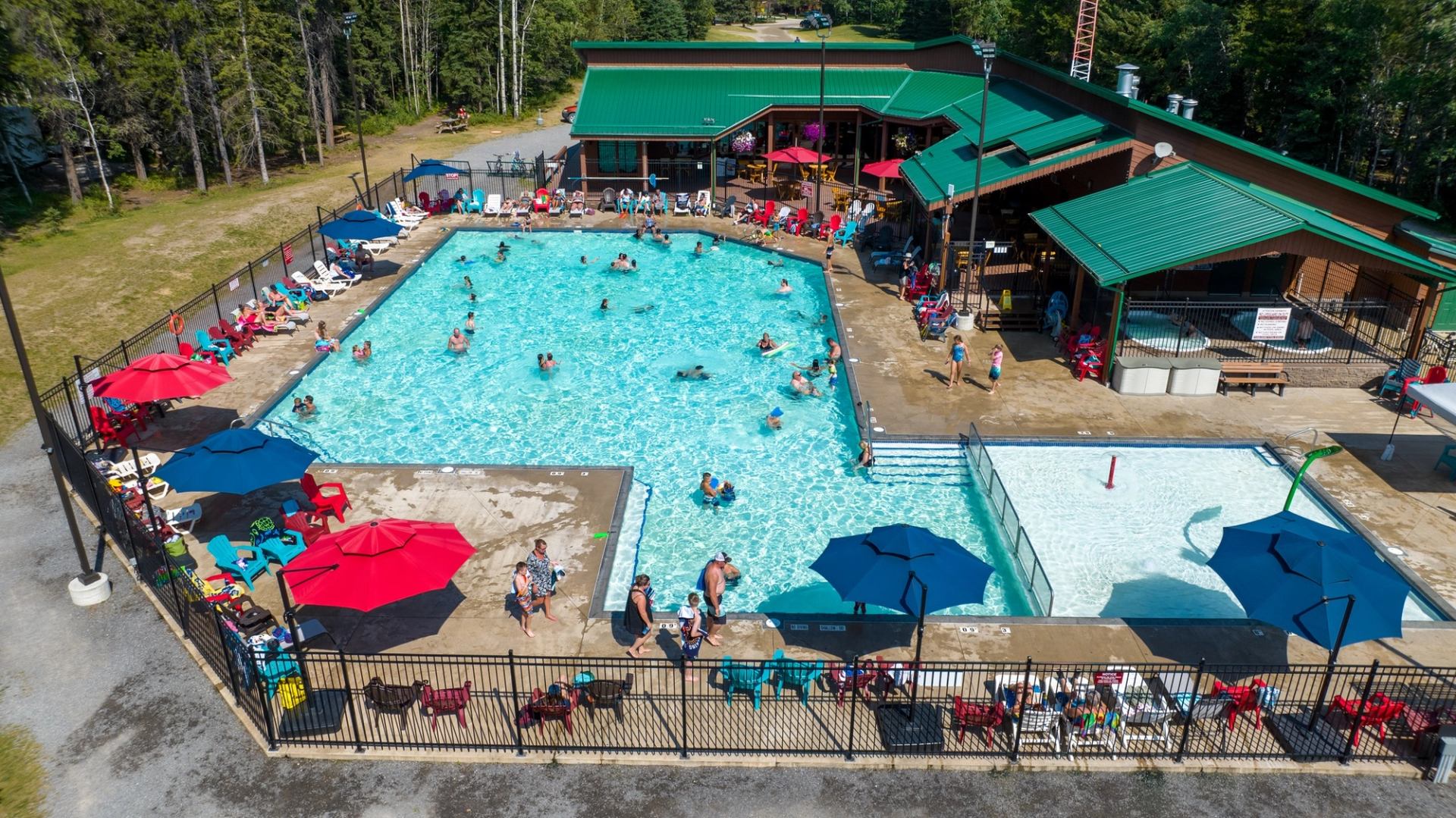 Outdoor swimming pools with people in water, lounge chairs and umbrellas beside green-roof building.