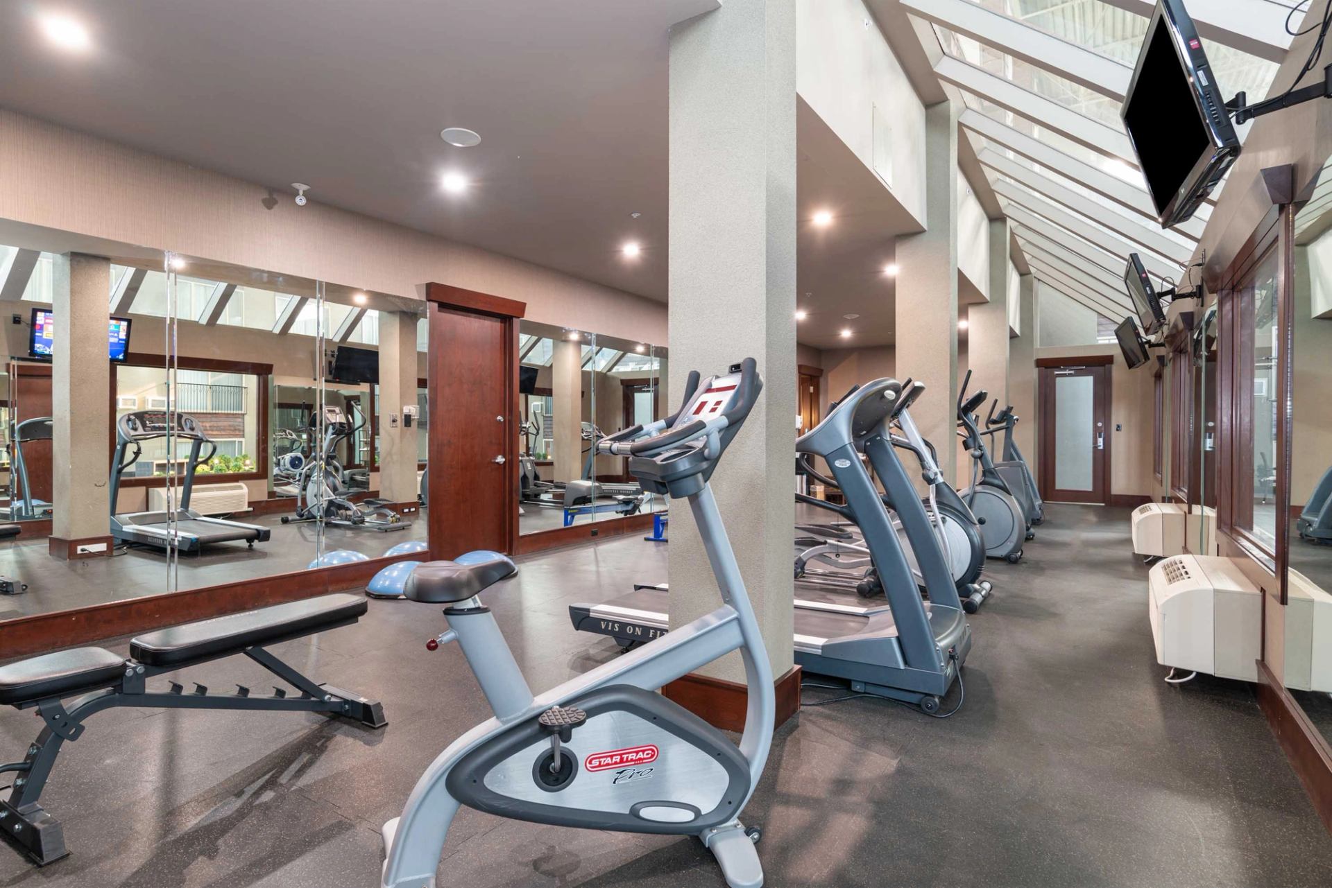 Hotel gym with treadmills, bikes, weights, and mirrored walls.