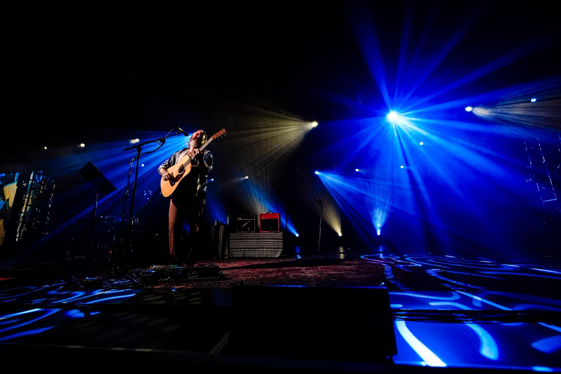 Artist playing guitar onstage under bright blue and gold concert lights