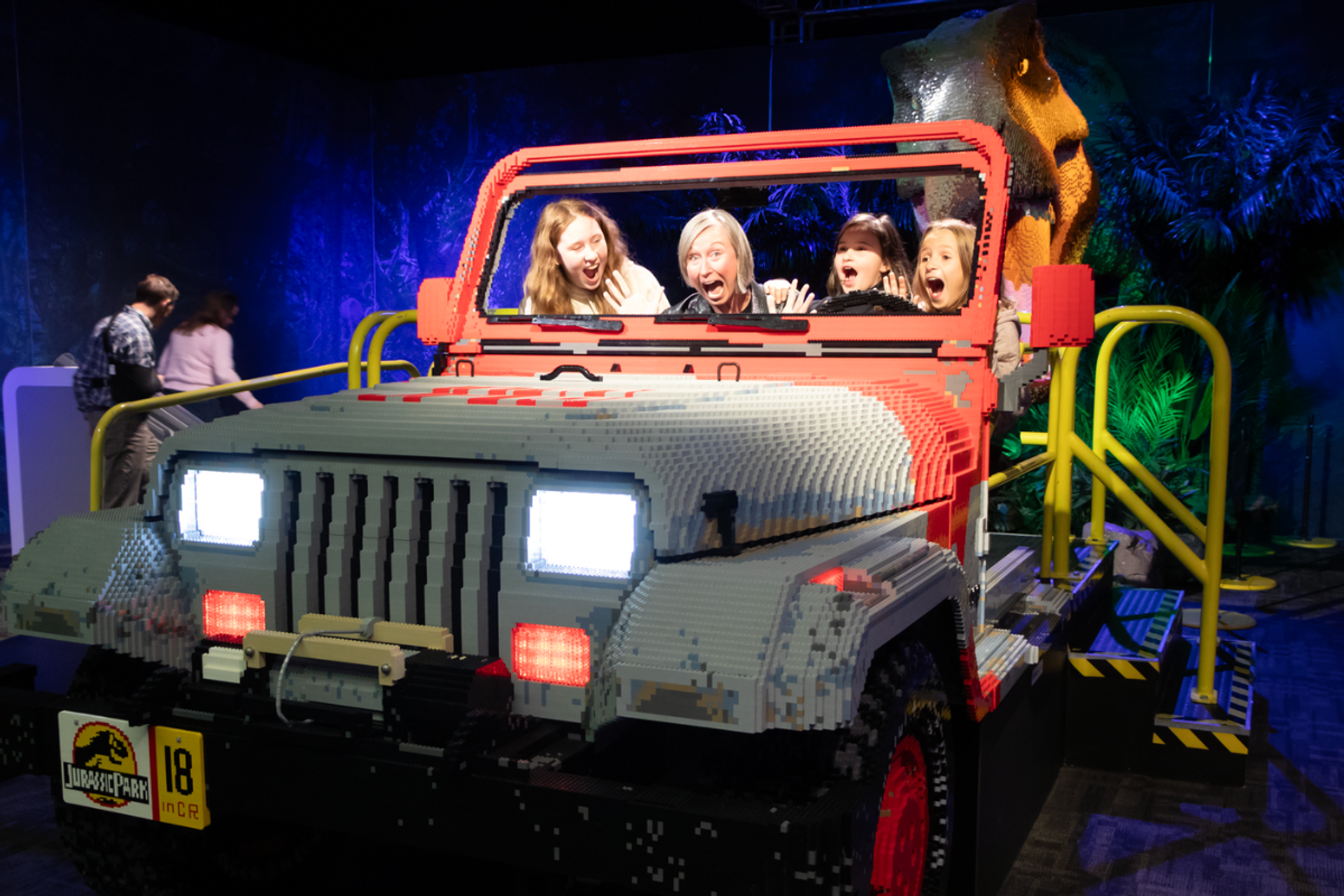 LEGO Jurassic World jeep with visitors and a dinosaur head in the background.