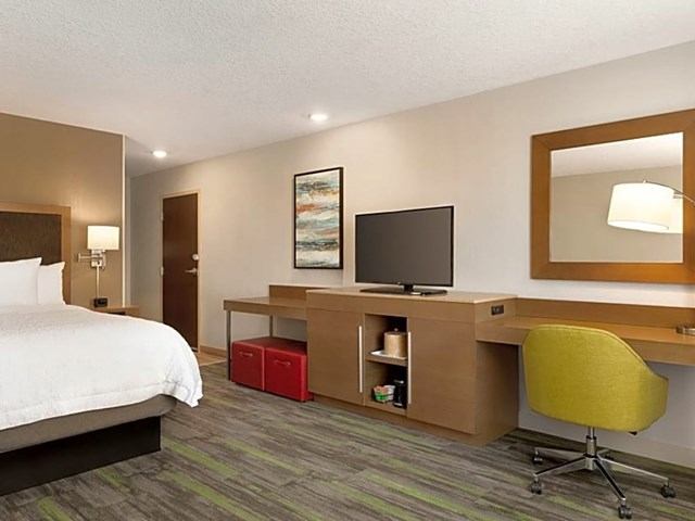 Modern hotel room with bed, desk, TV, and chair.