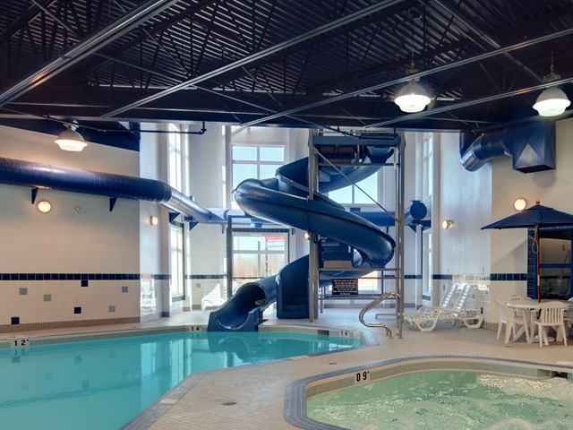 Indoor pool at Ramada Drayton Valley with slide, hot tub, and lounge chairs.