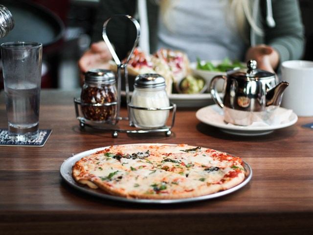 Pizza on plate with pepper shakers and teapot on restaurant table.