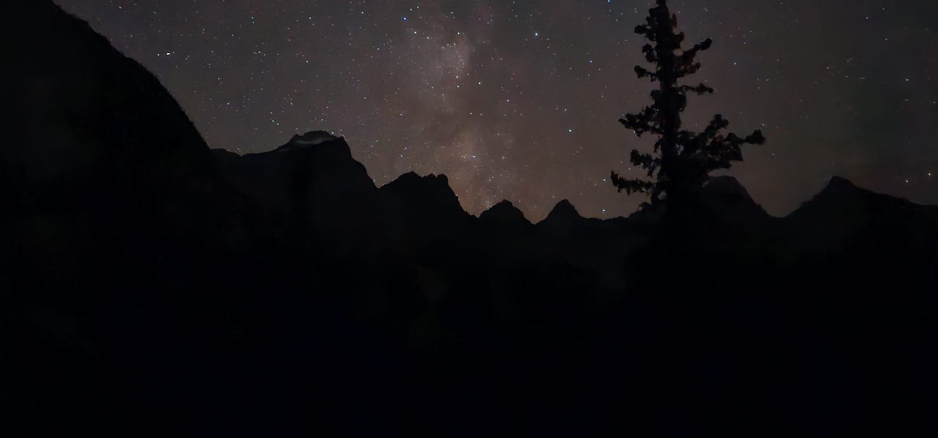Milky Way glowing above mountain silhouettes in the night.
