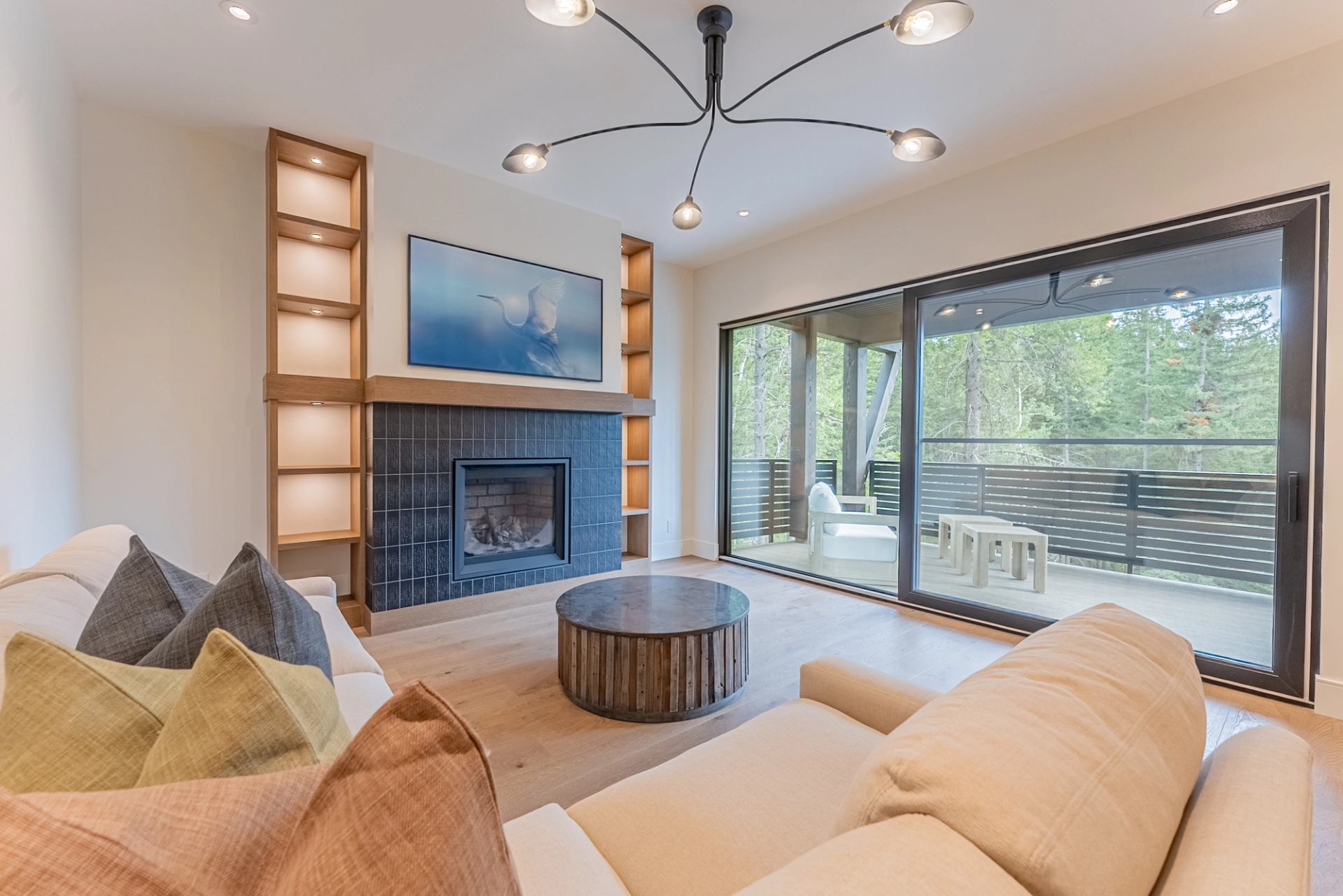 Living room with fireplace, built-in shelves and sliding doors overlooking a wooded balcony.