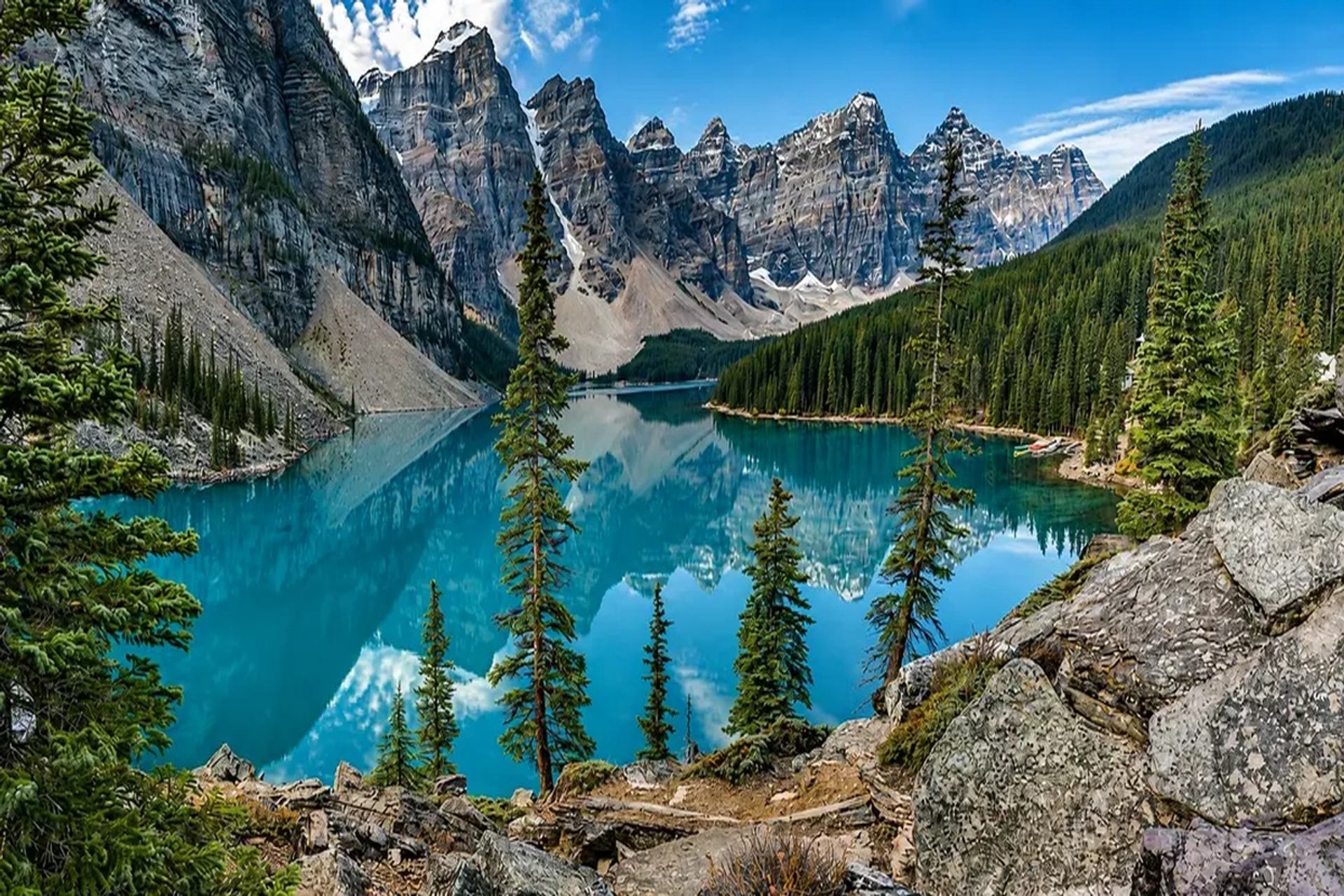 Turquoise mountain lake reflects rugged peaks, clouds and surrounding evergreen forest.