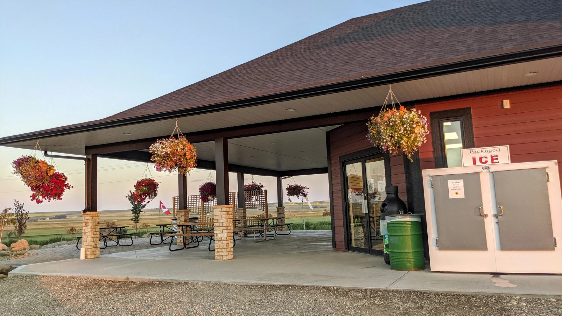 Storefront with flower baskets, 'Packaged Ice' sign, and picnic tables with a scenic view.