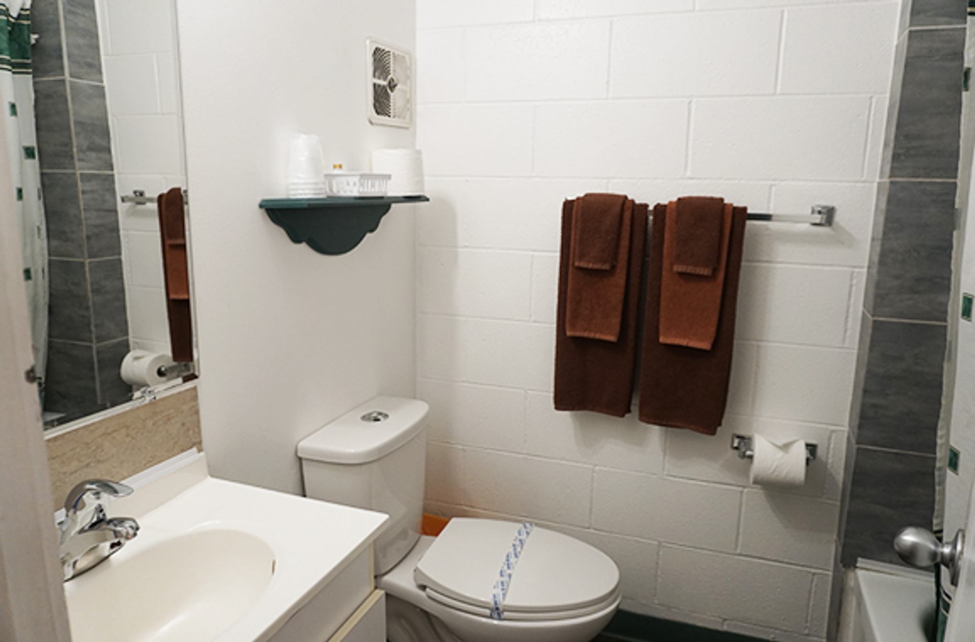 Small bathroom with sink, toilet, brown towels on rack and bathtub with shower curtain.