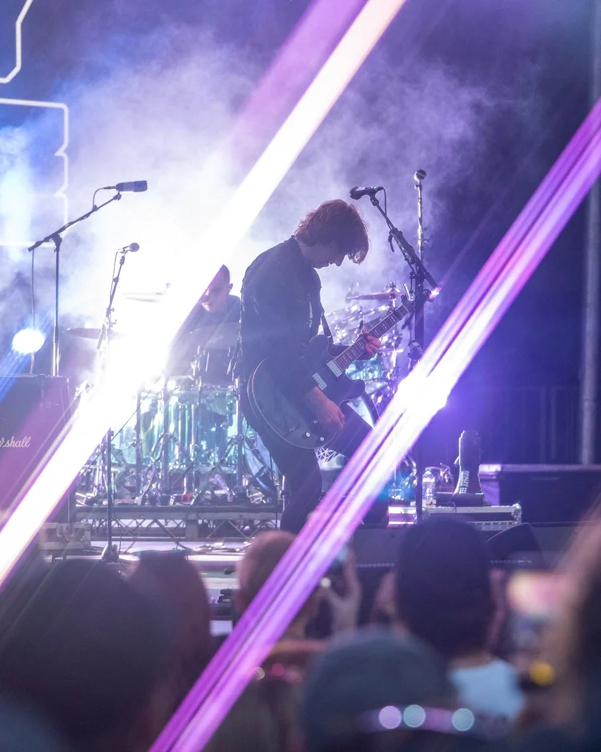 Guitarist performs on smoky stage with bright lights and lasers before concert crowd.