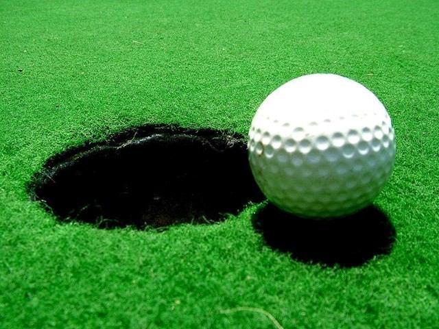 Golf ball teetering on the edge of the hole on a vibrant green.