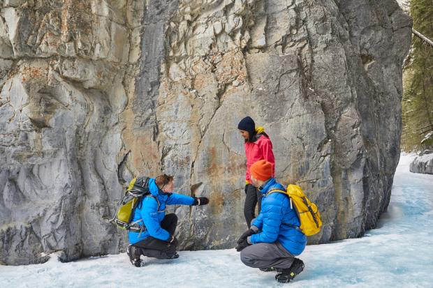 A group of three stop to explore the canyon walls while winter hiking through Grotto Canyon near Canmore in Kananaskis Country