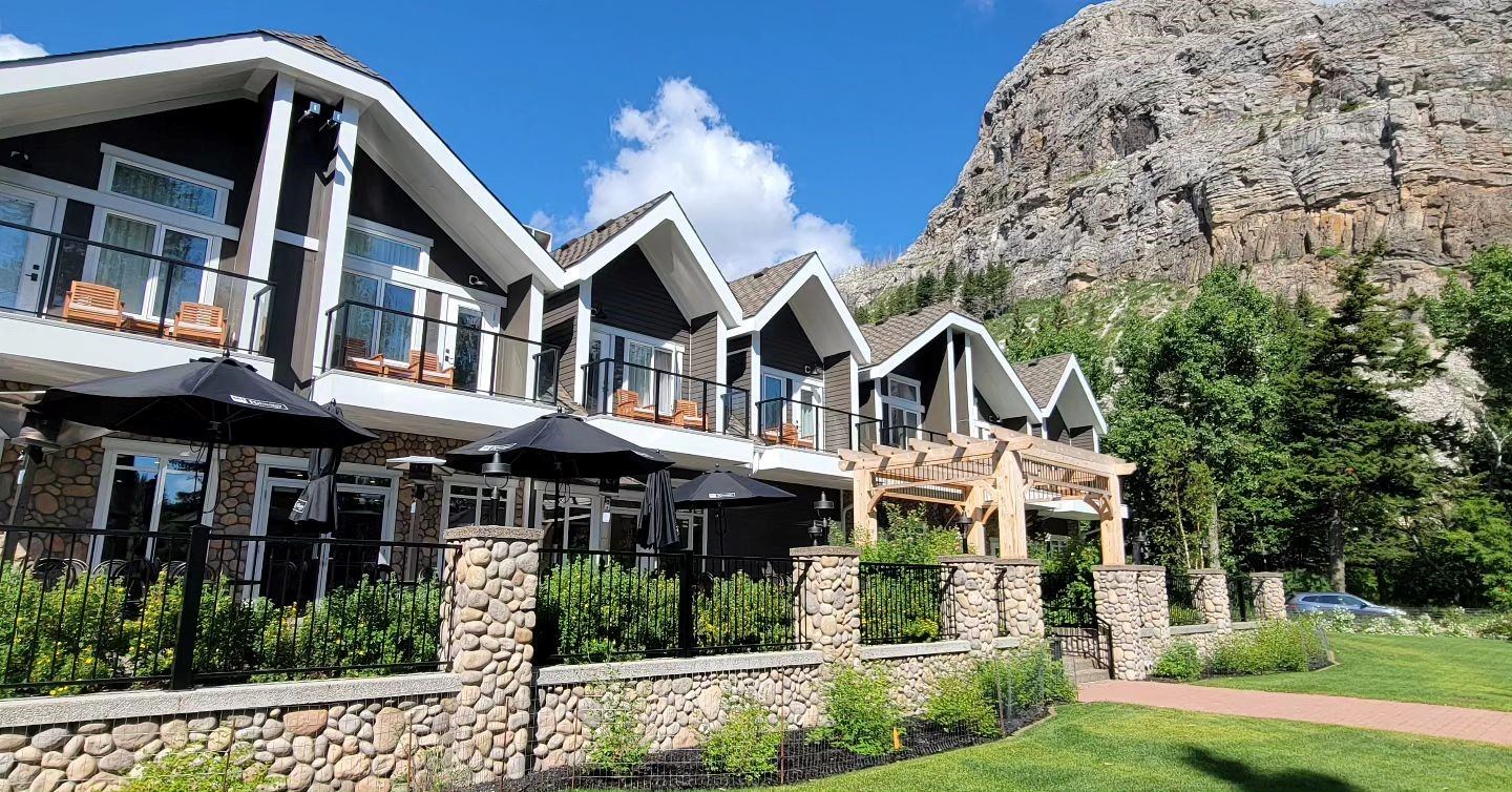 Scenic lodge with peaked roofs, stone pillars, balconies, and mountain backdrop.