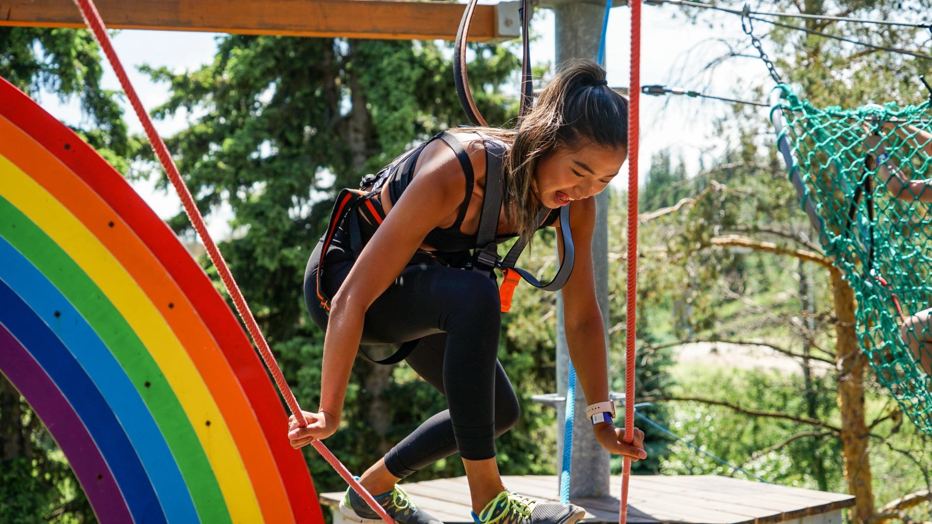 A young adult woman balances on a climbing tower obstacle.