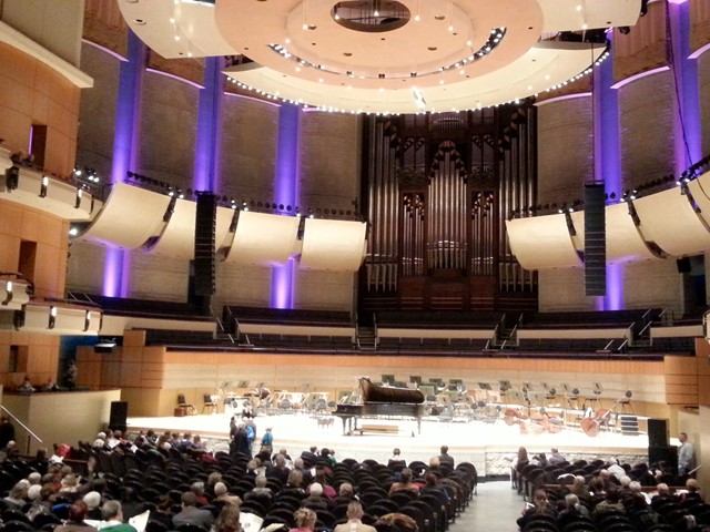 Theatre stage with pipe organ, musicians, and audience seating in rows.