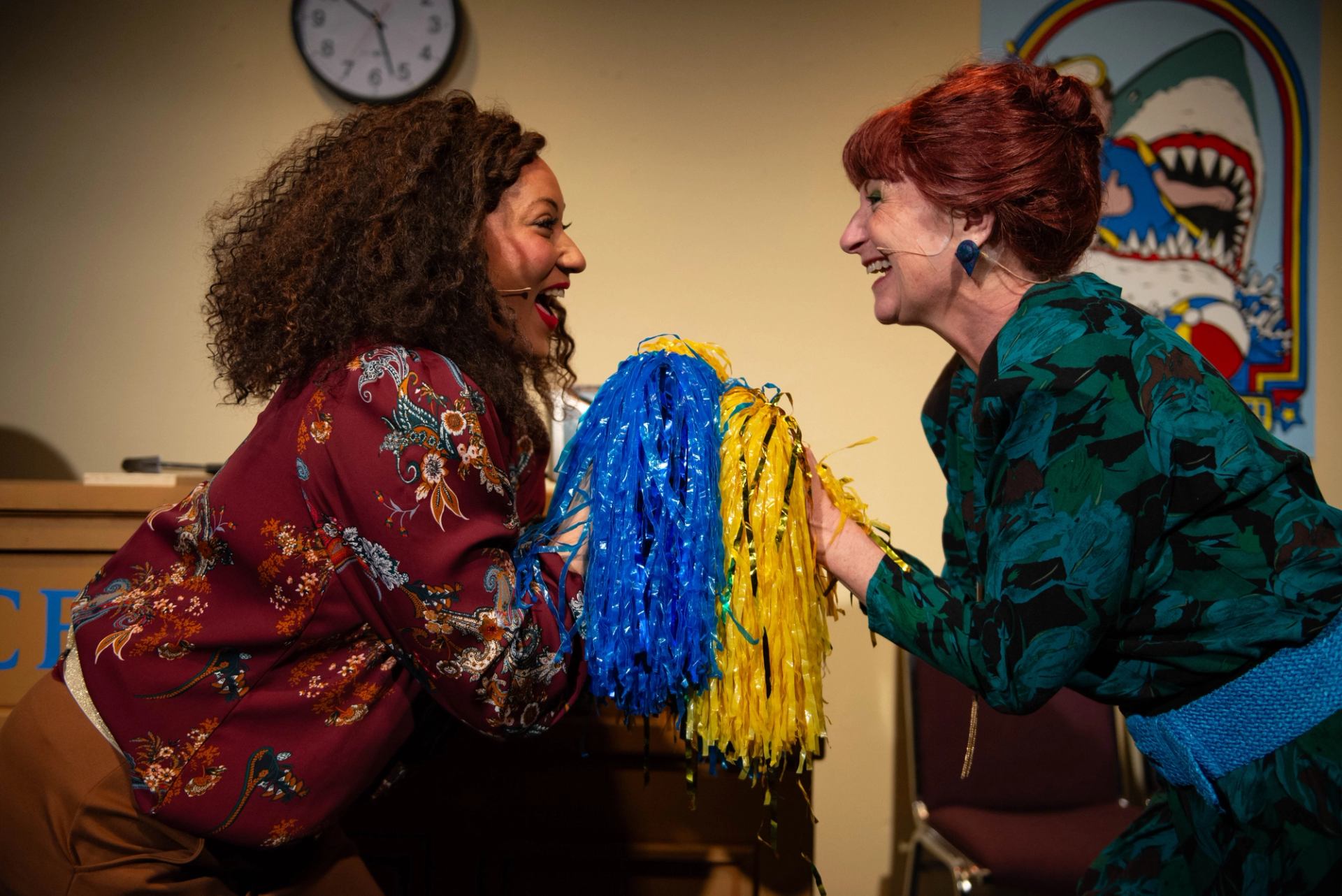 Two women holding pompoms, looking at each other smiling