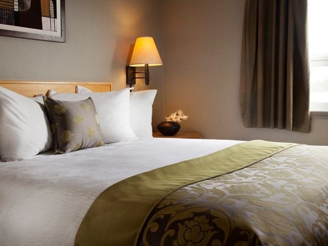 Cozy hotel bed with floral pillows, throw blanket, and warm lighting.