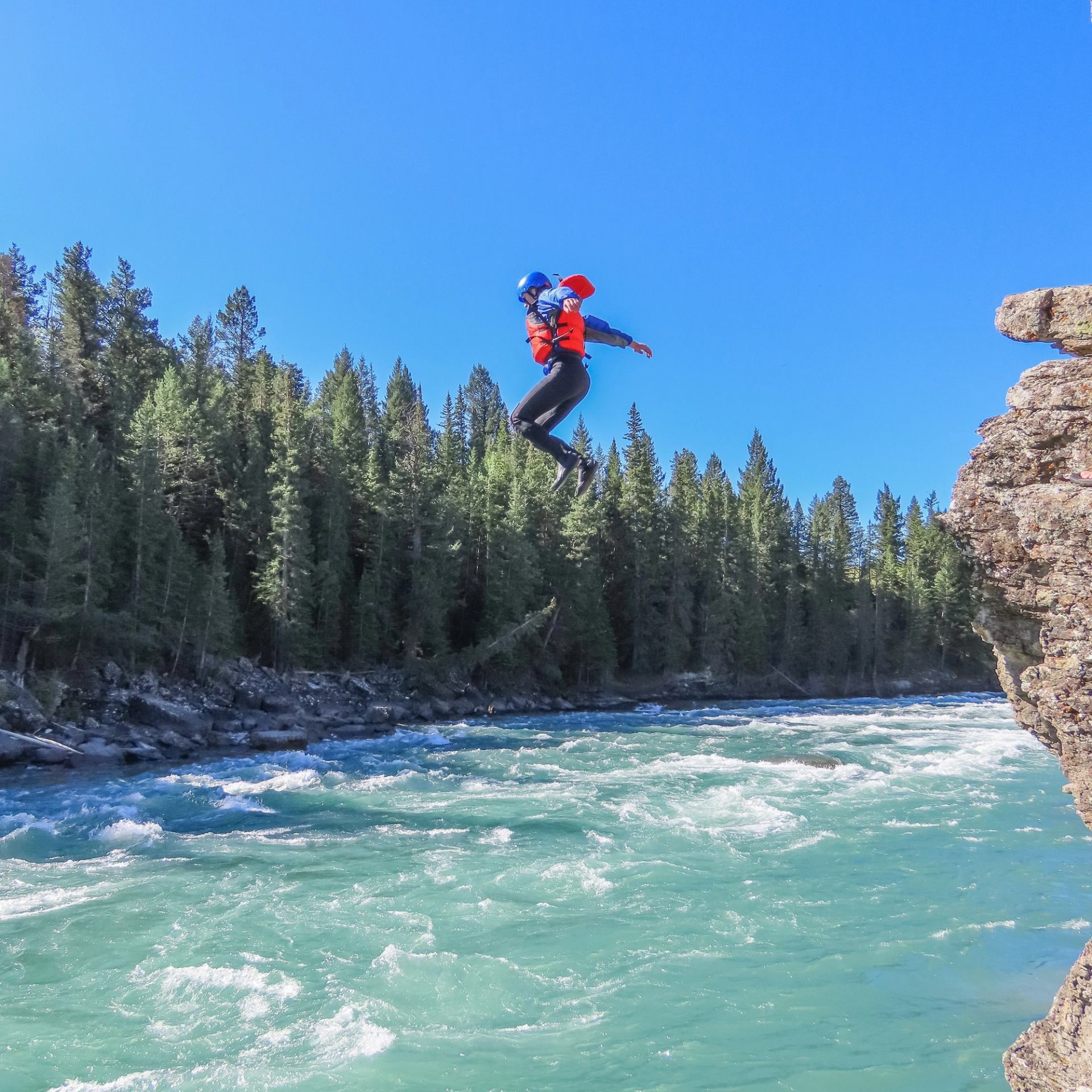Person in wetsuit, lifejacket and helmet, jumping off a cliff into the Bow River