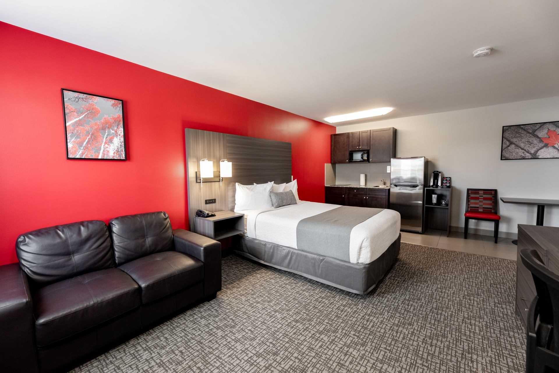 Guest room with bed, leather sofa, red accent wall and kitchenette.