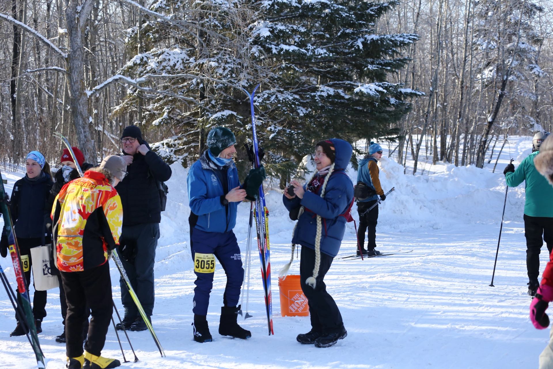Cross-country skiers in a snowy forest, standing with skis and poles near a race checkpoint.