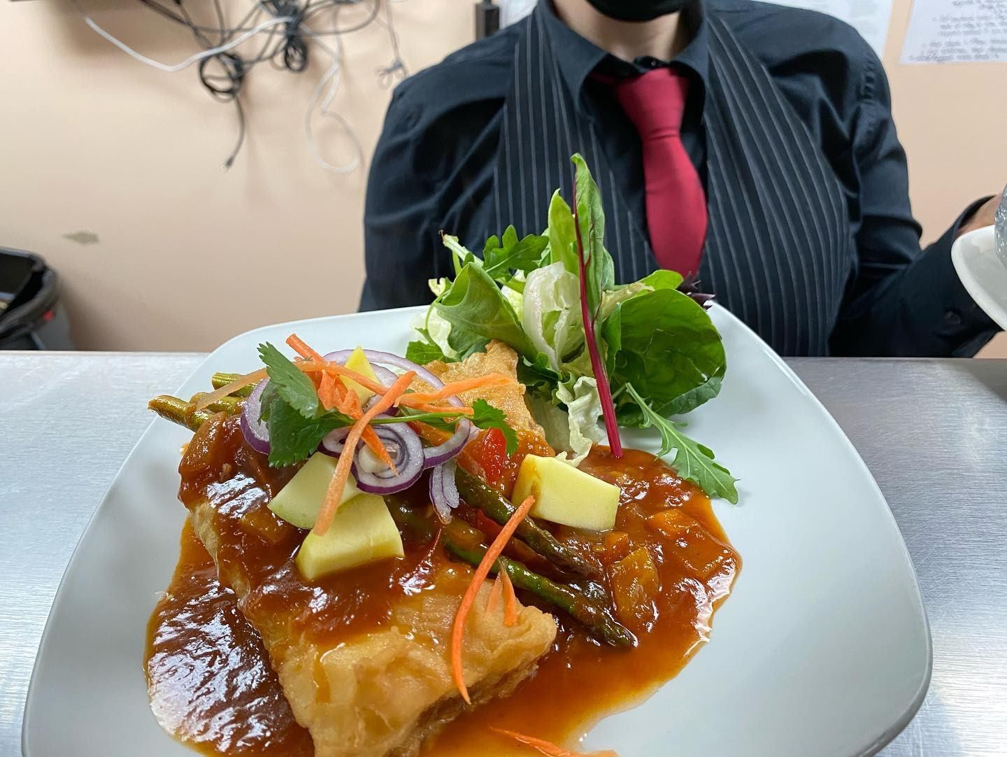 Plate of Thai dish topped with fresh herbs, vegetables, and rich sauce