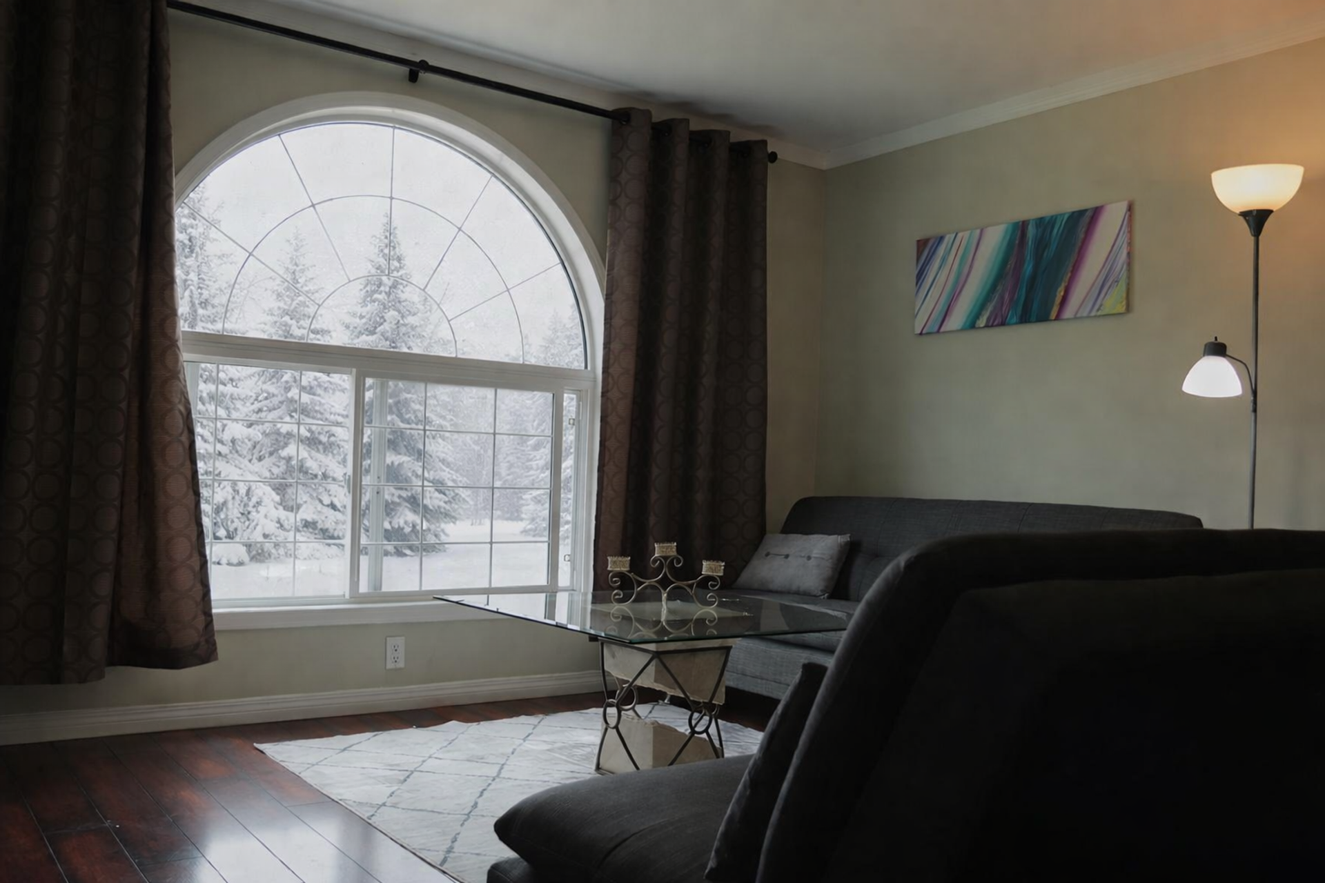 Living room with arched window, snowy trees outside, grey sofa and glass coffee table.