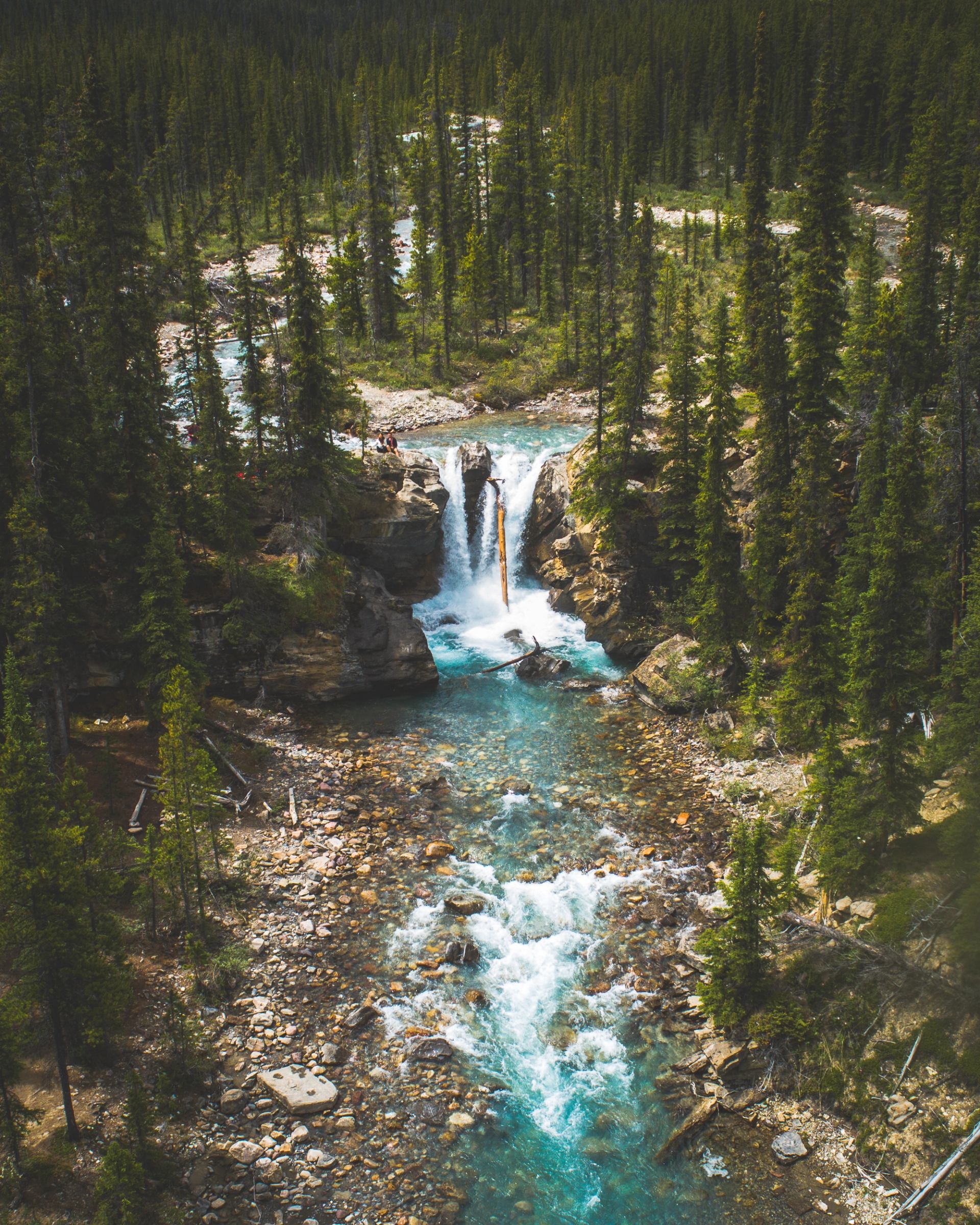 Aerial view of a turquoise waterfall flowing through a dense forest valley.