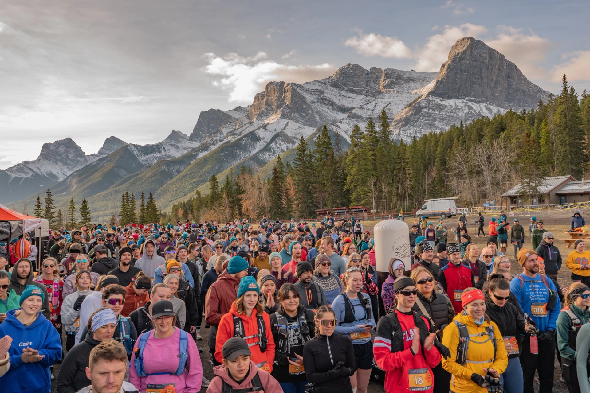 Large group of runners at a trail race with mountains and pine trees in the background.