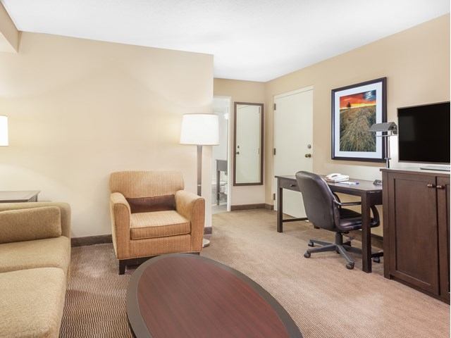 Hotel suite with armchair, sofa, coffee table, desk, and TV cabinet.