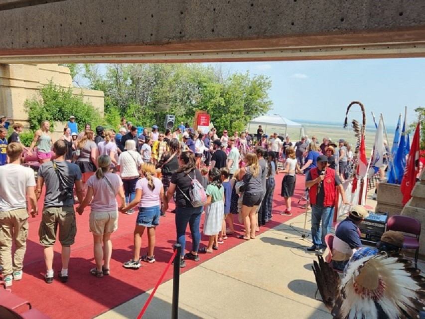 People holding hands on plaza with flags in background.