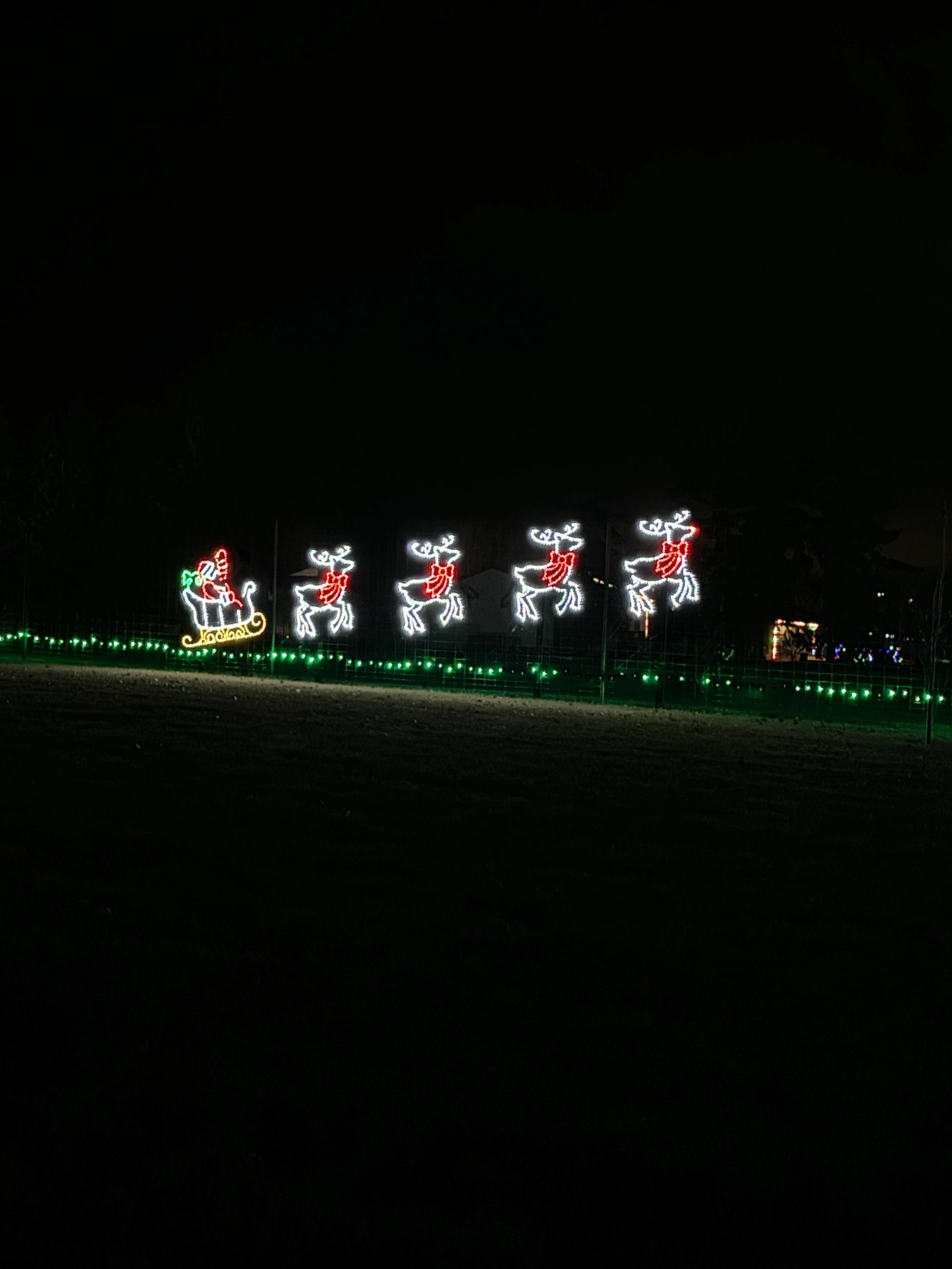 Illuminated Santa in sleigh pulled by four glowing reindeer against a dark night sky.