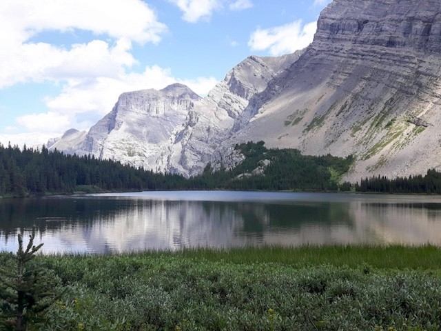 Mountain lake with forest shoreline and rocky peaks reflected in still water.