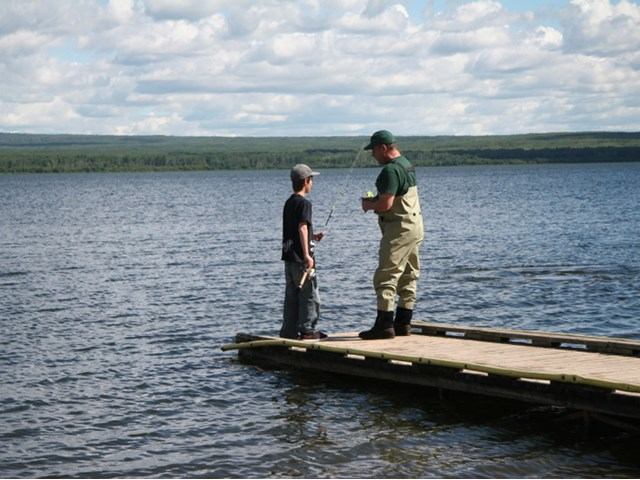 Two people standing on a dock fishing.