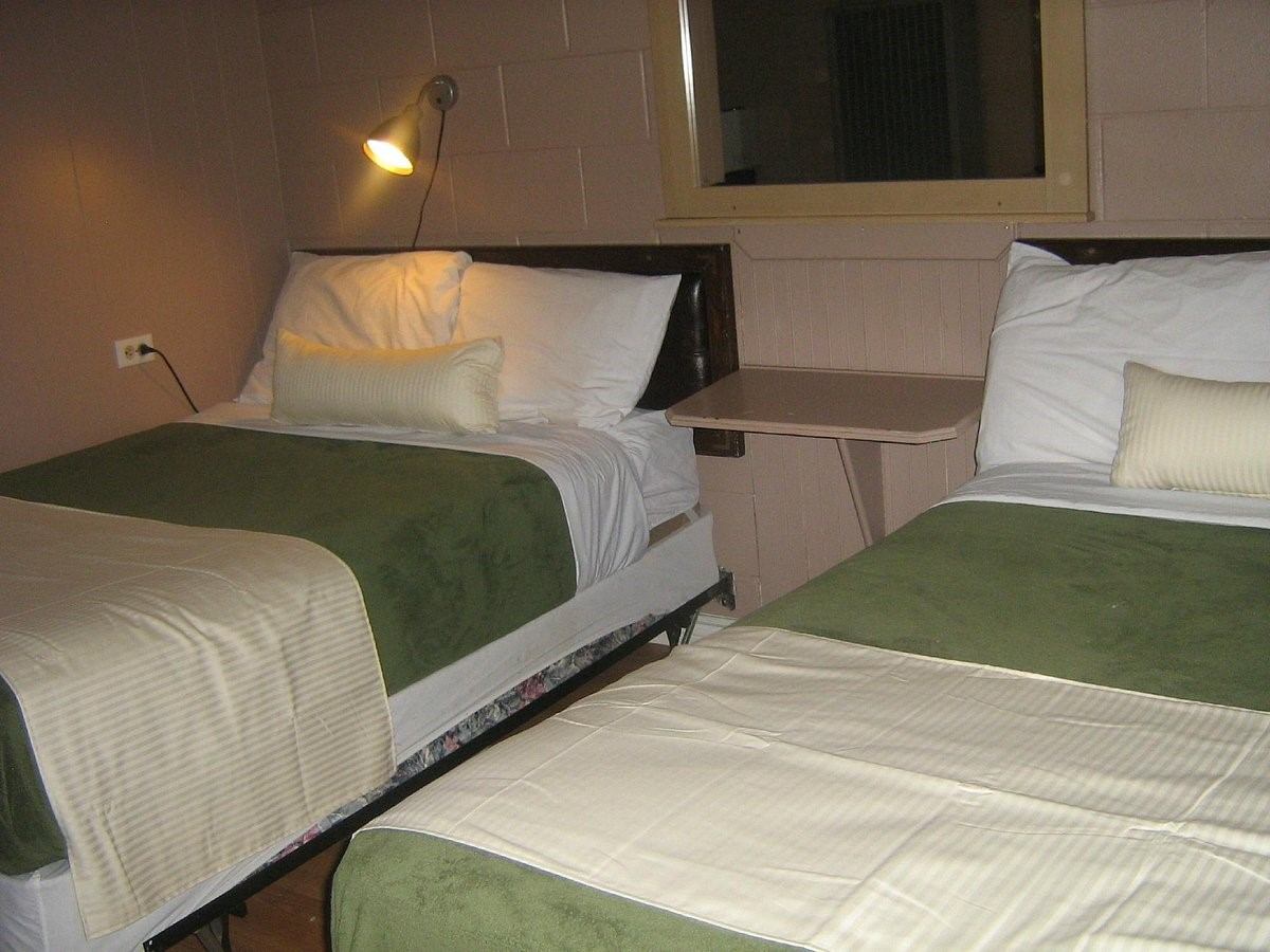 Motel room with two single beds, green blankets, and a wall-mounted reading light.